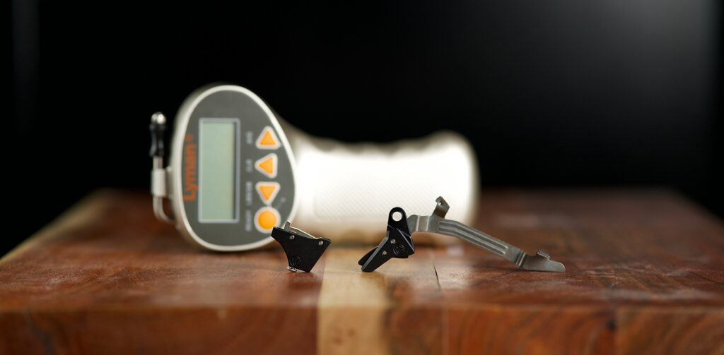a hair trigger on a table with a lyman trigger pull gauge behind it